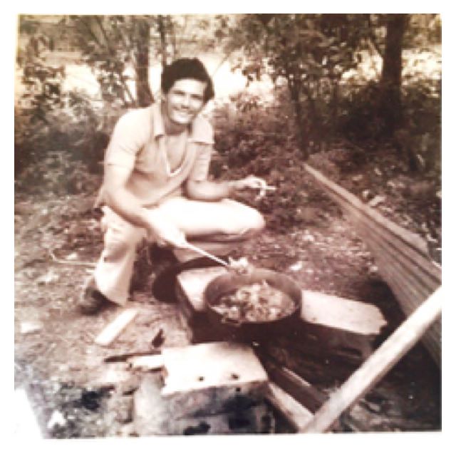 An image of Ismael, the author’s uncle, squating beside a fire cooking.